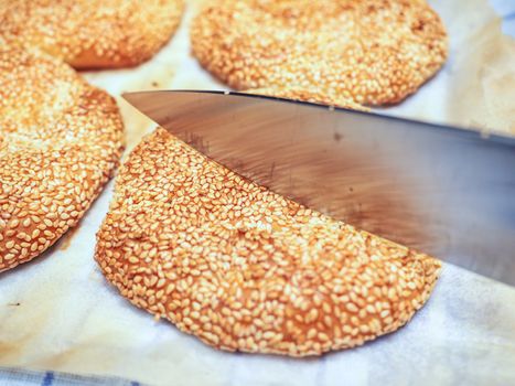 Fresh baked sesame bread being cut with a steel knife