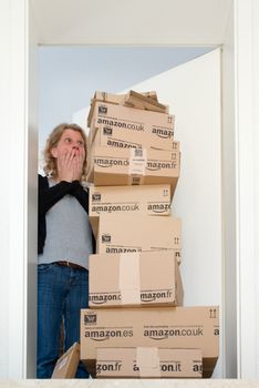 OSTFILDERN-SCHARNHAUSEN, GERMANY - MAY 18, 2014: A woman is horrified by a large stack of parcels by Amazon.com in different sizes waiting in front of the entrance door to her flat on May, 18, 2014 in Ostfildern-Scharnhausen near Stuttgart, Germany. This conceptual photo can serve different purposes: It might demonstrate the domination of Amazon.com in the area of online shopping or the trend in general to shop online for all the different items you need in your personal life.