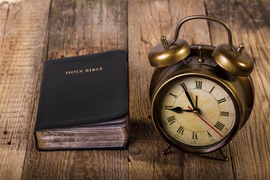 Holy Bible with clock on wood. Focus on clock.