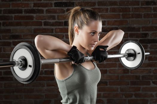 Portrait of Young fit woman lifting dumbbells on brick background 