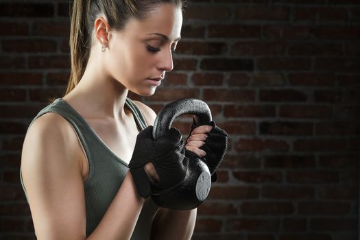 Portrait of Young fit woman lifting kettle bell on dark background 