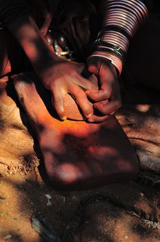 Himba woman grinding red ochre with a stone on another stone
