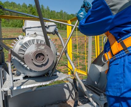 Worker repairing motor of the pumpjack. Center with a crowbar