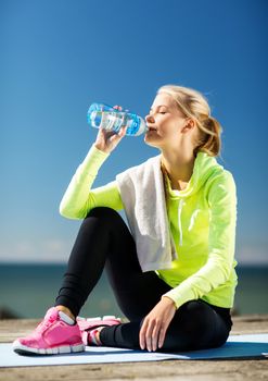 fitness and lifestyle concept - woman drinking water after doing sports outdoors