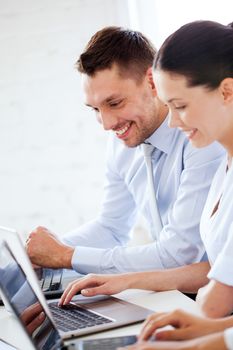 smiling businesswoman and businessman working with laptop in office