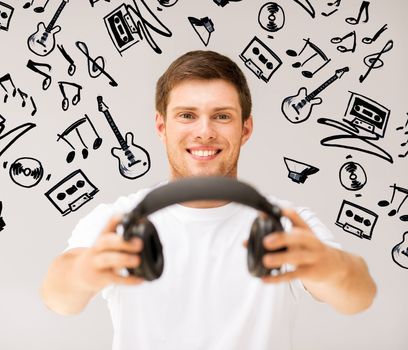music and technology - young smiling man offering headphones
