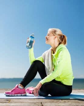 sport and lifestyle concept - woman drinking water after doing sports outdoors