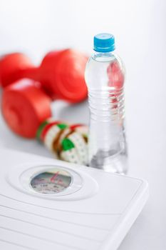 sport and diet concept - scales, dumbbells, bottle of water and measuring tape