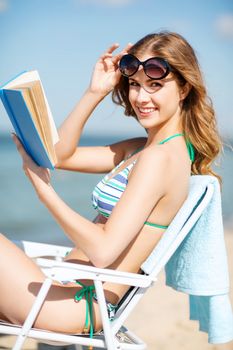 summer holidays and vacation - girl reading book on the beach chair