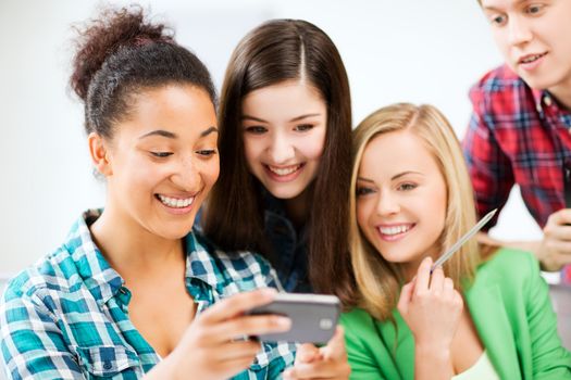 education and internet - smiling students looking at smartphone