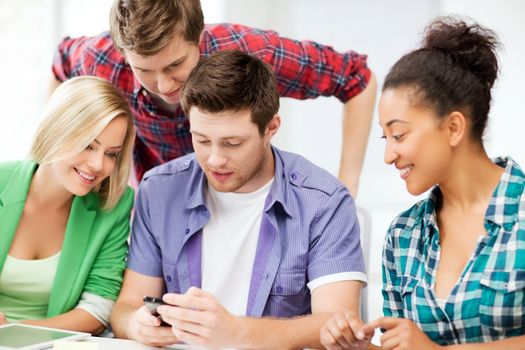 education, smatphones and internet - smiling students looking at smartphone at school