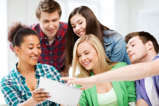 education, technology and internet concept - smiling students looking at tablet pc at school