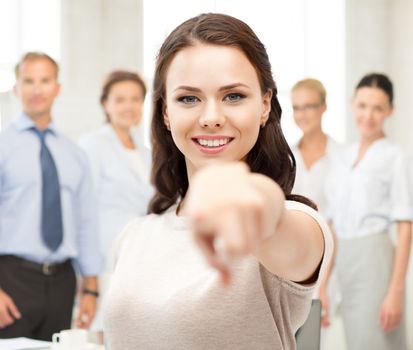 business concept - attractive young businesswoman pointing at you in office