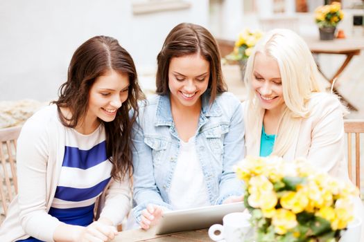 holidays, tourism and internet - beautiful girls looking at tablet pc in cafe outside