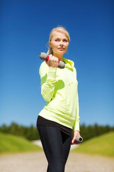 sport and lifestyle - young sporty woman with light dumbbells outdoors