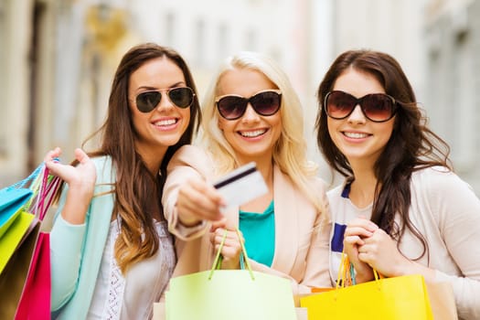 shopping and tourism concept - beautiful girls with shopping bags and credit card in ctiy