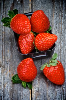 Heap of Perfect Raw Strawberries in Square Shape Black Bowl isolated on Rustic Wooden background. Top View