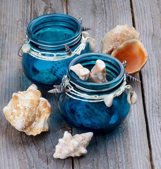 Collection of Sea Shells and Corals in Blue Glass Jars closeup on Rustic Wooden background