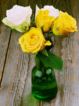 Bouquet of Yellow and White Roses with Droplets in Green Glass Vase closeup on Rustic Wooden background