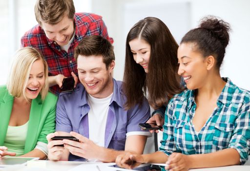 education, technology and internet - smiling students looking at smartphone at school