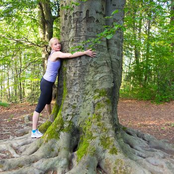 Relaxed young lady embracing a tree receiving life energy from the nature.