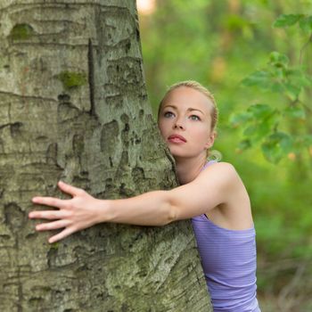 Relaxed young lady embracing a tree receiving life energy from the nature.