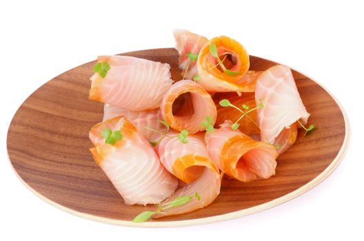 Snack of Swirled Slices of Delicious Smoked Sturgeon with Fresh Greens on Wooden Plate isolated on white background