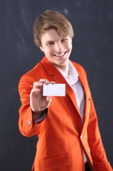 Portrait of a young, handsome man in the orange jacket standing on black background plate holding a business card with space for your text