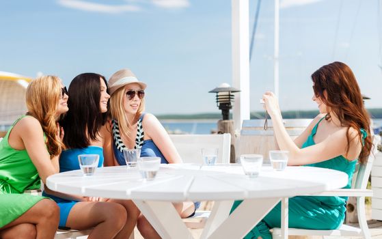 summer holidays and vacation - girls taking photo with digital camera in cafe on the beach