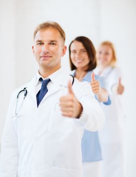 healthcare and medical concept - male doctor with stethoscope and colleagues showing thumbs up