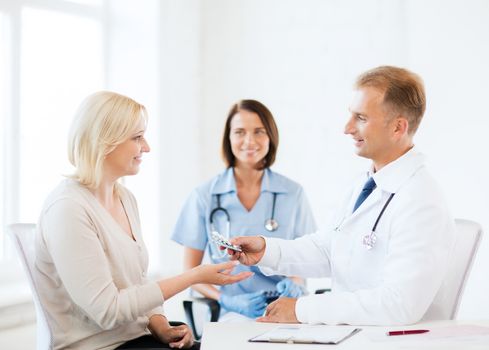 healthcare and medical concept - doctor giving tablets to patient in hospital