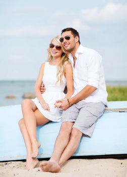 summer holidays and dating concept - couple in shades sitting at sea side