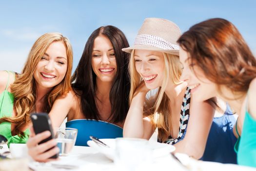 summer holidays, vacation and technology - girls looking at smartphone in cafe on the beach