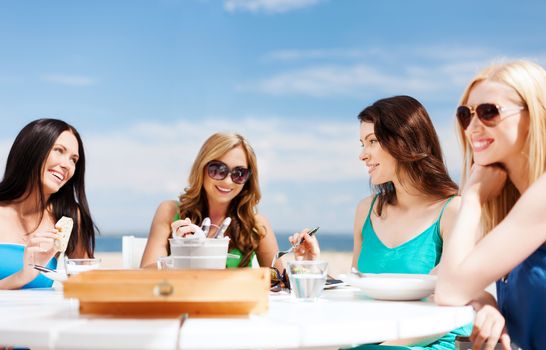 summer holidays and vacation - girls eating and drinking in cafe on the beach