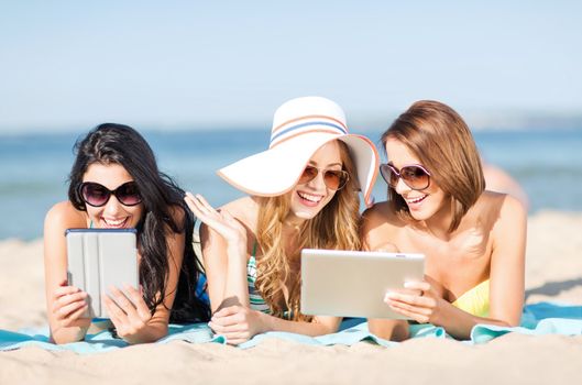 summer holidays, technology and internet concept - girls in bikinis with tablet pc sunbathing on the beach