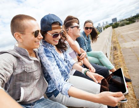 summer holidays, teenage and technology concept - group of teenagers looking at tablet pc