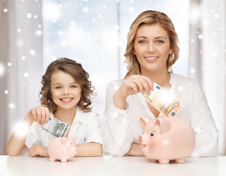 banking, finances, investment and happy people concept - mother and daughter with piggy banks and paper money