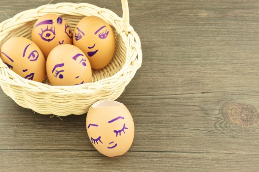Happy and fun emoticons on empty eggshell in basket with wood background.