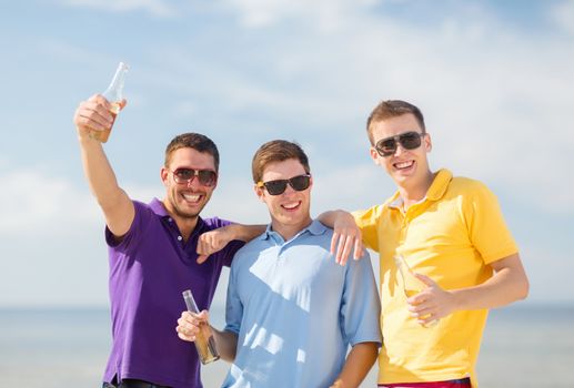 summer, holidays, vacation, happy people concept - group of friends having fun on the beach with bottles of beer or non-alcoholic drinks