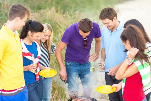 summer, holidays, vacation, happy people concept - group of friends having picnic and making barbecue on the beach