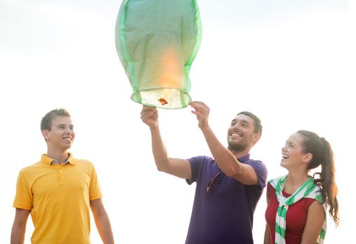 summer, holidays, vacation, happy people concept - group of friends with chinese sky lanterns on the beach