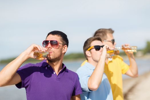 summer, holidays, vacation, happy people concept - group of friends having fun on the beach with bottles of beer or non-alcoholic drinks