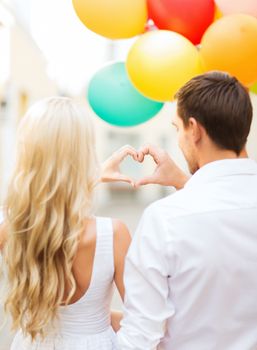 summer holidays, celebration and dating concept - couple with colorful balloons making heart shape in the city