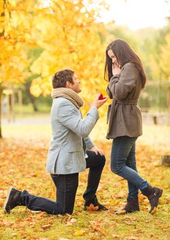 holidays, love, couple, relationship and dating concept - kneeled man proposing to a woman in the autumn park