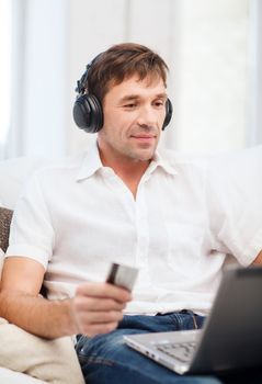 technology, leisure and lifestyle concept - happy man with headphones and credit card listening to music at home