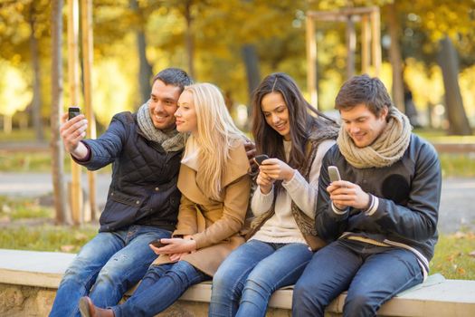 summer, holidays, vacation, happy people concept - group of friends or couples with smartphone having fun in autumn park