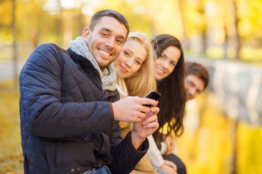 summer, holidays, vacation, happy people concept - group of friends or couples with smartphone having fun in autumn park