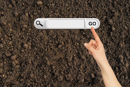 Human hand indicates the search bar in browser. Cultivated brown soil surface on background