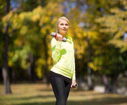 sport and lifestyle concept - young sporty woman with light dumbbells outdoors