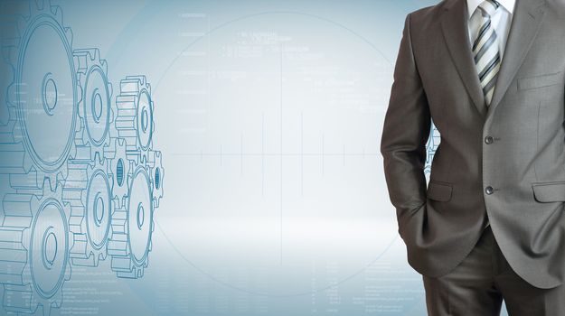 Businessman standing with hands in pockets. High-tech wire frame gears and graphs at backdrop